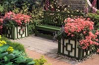 pelargoniums in matching Versailles tubs either side of green wooden painted bench