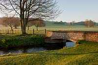 stream stone bridge parkland bare trees grass sheep view sun sunny blue sky south downs West Dean college Sussex rural country