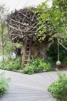 The RHS Back to Nature Garden  – tree house made from wood and tree branches, wooden ladder made from tree slab, rope swing, wooden decking board walk, planting of ferns and shade loving plants - Designer: HRH The Duchess of Cambridge with Andree Davies and Adam White - Sponsor: The RHS 