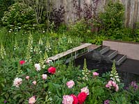 The Roots in Finland Kyrö Garden with dense planting of Digitalis purpurea and Red and Pink Peonies surround a sunken patio area.- Designer: Taina Suonio - Sponsor: Kyrö Distillery Company Ltd. RHS Chelsea Flower Show 2019