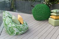 View of rooftop garden with timber deck, bean bags, cushions and woven willow green apple sculpture. The Greenfingers Charity Garden. Designed by Kate Gould Gardens, sponsored by Greenfingers Charity, RHS Chelsea Flower Show, 2019.
