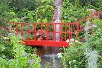 The Trailfinders 'Undiscovered Latin America' Garden at RHS Chelsea Flower Show 2019. View of the bright red brige and water fall over a stream. Design: Jonathan Snow. Sponsor: Trailfinders