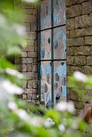 The Warners Distillery Garden, hand crafted glass panel with blue tint created from copper reacting withthe glass, inspired by the distillation process, designed by Wendy Newhofer - Design: Helen Elks-Smith - Construction: Bowles and Wyer - Sponsor: Warners Gin. 