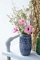 Spring bouquet of Chamelaucium and pink Eustoma in a ceramic vase alongside an ethnic jewellery stand.
