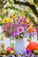 Metal jug of autumn flowers: asters, hydrangea, dahlia, cosmos, rudbeckia, sedum, solidago and chrysanthemum.