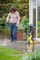 Woman pressure washing a patio with a jet spray. 