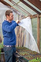 Man preparing a greenhouse for winter - putting up bubble wrap insulation