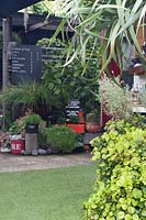 A chalkboard cafe menu behind an ecclectic group of pots and containers used for plants, including a red metal fire bucket, Australia. 
