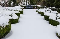 Avenue of Box 'eggcups' in the vegetable garden with view to the seat. Garden in snow
