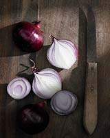 Allium cepa - onions - and knife on wooden surface 
