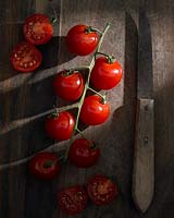 Solanum lycopersicum -tomato - and knife on wooden surface. 