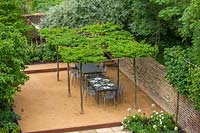 Patio with dining area, covered with pleached tree canopy. 
