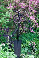 Metal sculpture sits in mixed border. 