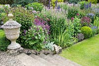 Herbaceous border with lawn stone steps and old stone urn, Scotland â€‰ 