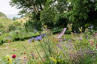 View over flowering perennial border to deckchair on the lawn. 