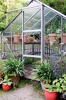 View of metal framed Greenhouse with symmetrically arranged pots around its door.