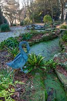 Pond with duckweed and ferns with metal 'Swan' statue, West Sussex