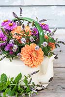 Old teapot with orange dahlias, mint flowers and asters