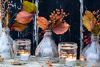 Autumn floral arrangement with beech leaves and rosehips in glass bottles with tealights