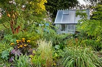 View of greenhouse among perennial grasses, shrubs and trees. 