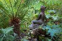 Statue of mermaid surrounded by bold foliage. 