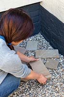 Woman placing small paving in gravel courtyard. 