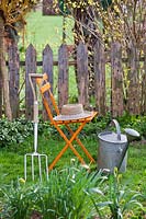 Seat with hat, watering can and fork in a garden setting