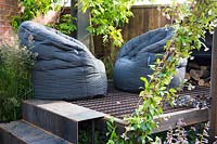 Modern beanbags on a raised metal platform surrounded by vines and a climber Trachelospermum jasminoides in industrial style summer garden