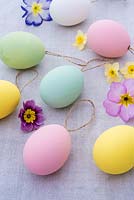 Pastel coloured easter eggs with string on linen background with spring flowers. 