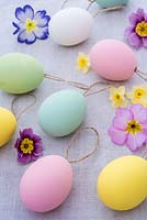 Pastel coloured easter eggs with string on linen background with spring flowers. 