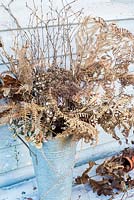 Selection of sprayed gold dried seedheads, ferns, berries and leaves displayed in florist's bucket