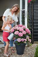 Woman and girl spending time together on patio whilst watering hydrangea in pot