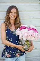 Woman holding glass vase of cut peonies