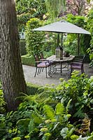 Table, chairs and parasol under shade of mature trees.