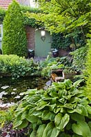 Courtyard with a small pond surrounded by flowerbeds, which include Alchemilla mollis, Hosta and Heuchera