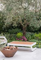 Contemporary seating with table and fire pit, overlooking large olive tree  - 'On Point' Garden, Ascot Spring Garden Show, 2018. 