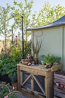 Potting bench next to a painted garden building with potted herbs  