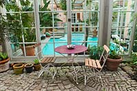 Bistro table and chairs sit in front of indoor swimming pool. Marina WÃ¼st garden, Germany. 