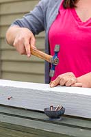 Close up detail of woman using a hammer to hammer copper nails into wooden post. 