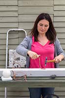 Woman using hammer to nail copper wire pot holders to wooden post. 