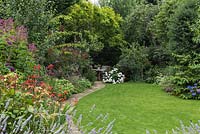 Town garden with key features of lawn, flower border and private seating area thanks to mature trees and shrubs

