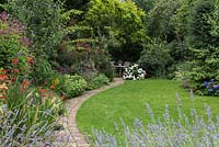 Town garden with lawn, flower border and path to private seating area shaded by trees and shrubs
