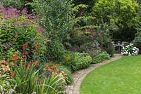 Curved brick path leads to a shady seating area.
A mixed border with herbaceous plants such as Eupatorium, Crocosmia and Sedum
