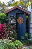 Grey painted outhouse with tropical plants in Australian garden.