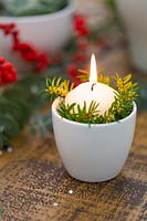 Candle in white pot with foliage decoration.