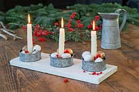 Table centrepiece of candle holders featuring painted walnuts and Ilex berries. 