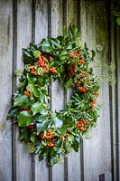 Autumnal wreath with Hedera helix and Pyracantha berries on wooden door in rustic setting.
