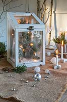 Festive arrangement using pine foliage and cones, LED lights, candles and baubles in rustic setting. 