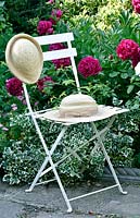 Chair holding vintage straw hats in front of flowering perennial border. 