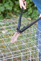 Close up detail of using bolt cutters to cut gabion basket to shape